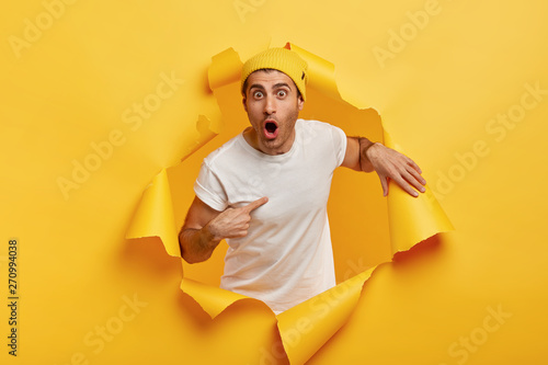 Foto Who, me? Stupefied emotional man points at himself, dressed in casual white t shirt, keeps mouth widely opened, cannot believe in astonishing news, isolated over yellow background