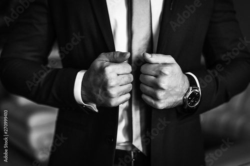 Man in business suit. A man puts on a suit. Close-up business stylish man buttoning his jacket. A businessman in an expensive suit.  Black and white photo