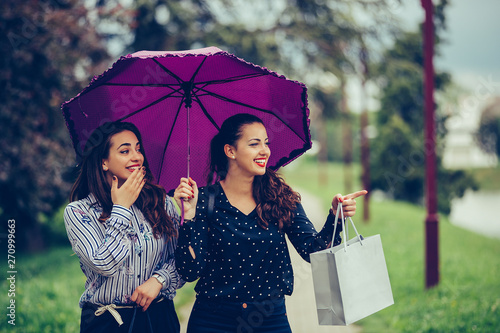 Two beautiful women walking in the park with umbrella above head photo