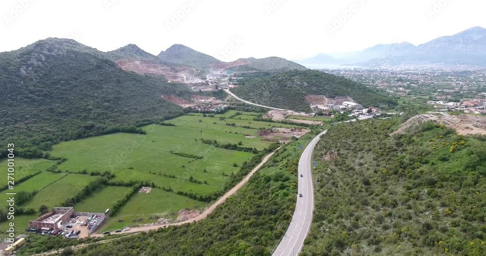 Quadcopter flight over the mountain valley. View of the green fields, rooftops of a little village and its winding roads with cars and other transportation traveling on the road Quadcopter flight over the mountain valley. View of the green fields, rooftops of a little village and its winding roads with cars and other transportation traveling on the road