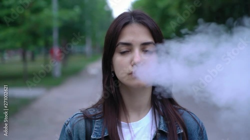 cool young girl smoking e-cigarette on the street in the park. Portrait of vaping person