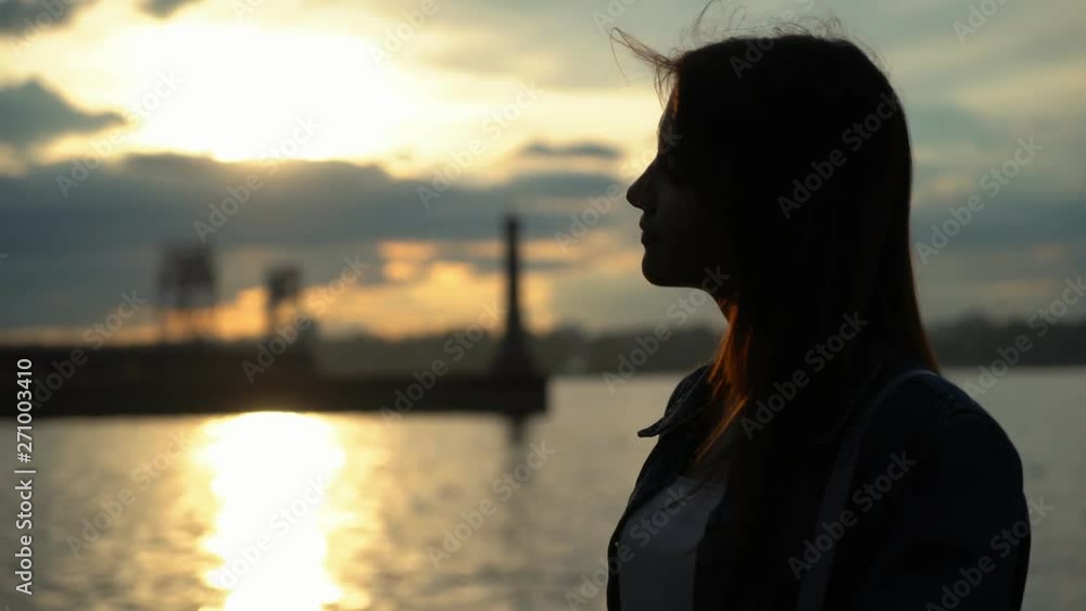 silhouette of cute smiling young girl near the water on the quay at sunset silhouette of cute smiling young girl near the water on the quay at sunset