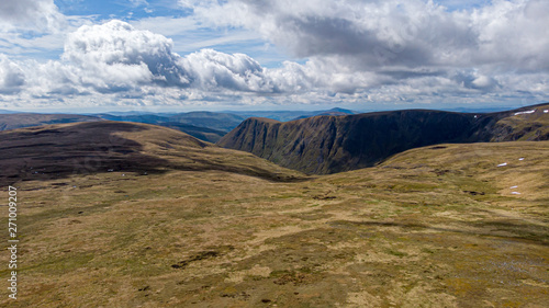 An aerial view of a Scottish mountain cliff with heather in the foreground under a majestic blue sky and huge white clouds photo