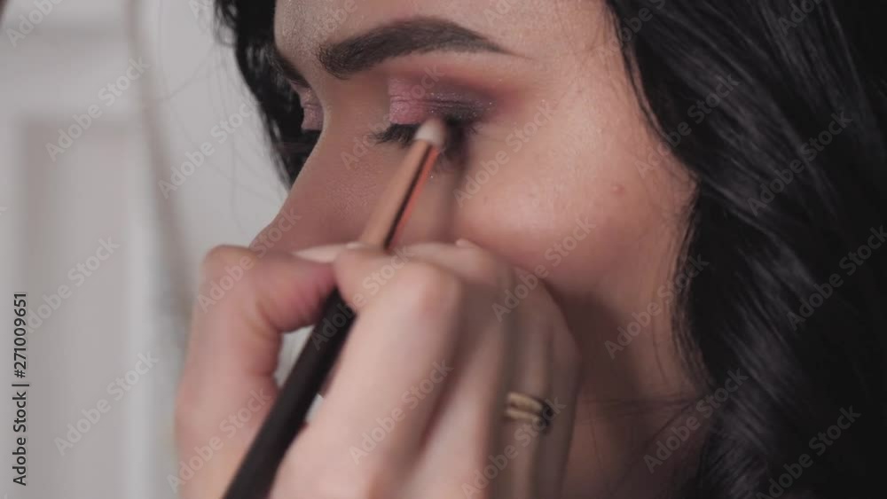 Closeup shot of cheerful young female makeup artist enjoying working with a beautiful young brown haired model, applying fresh trendy makeup on her eyes with long eyelashes, perfect brows using pencil Closeup shot of cheerful young female makeup artist enjoying working with a beautiful young brown haired model, applying fresh trendy makeup on her eyes with long eyelashes, perfect brows using pencil