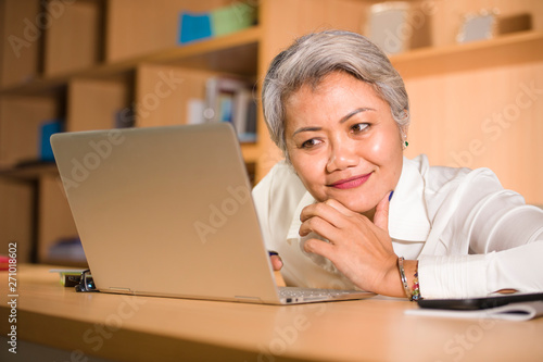 lifestyle office portrait of attractive and happy successful middle aged Asian woman working at laptop computer desk smiling confident in entrepreneur business success