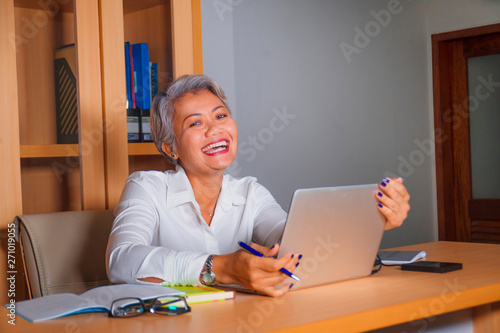 attractive and happy successful middle aged business Asian woman working at laptop computer desk smiling confident in entrepreneur celebrating success