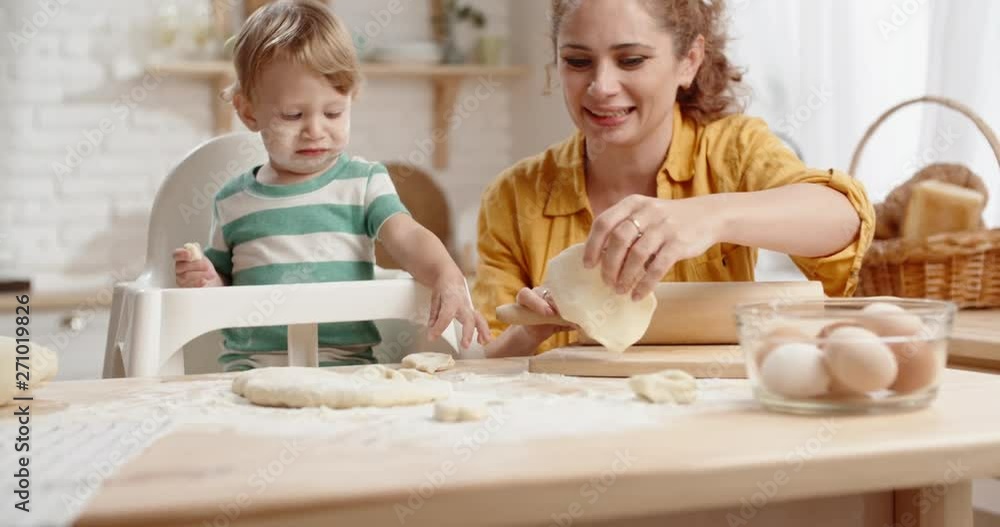 Young mother looking after her child, playing with him while making dough and cooking lunch - family ties concept close up Young mother looking after her child, playing with him while making dough and cooking lunch - family ties concept close up