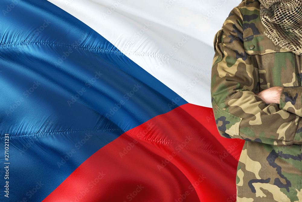 Φωτογραφία Crossed arms Czech soldier with national waving flag on background - Czech Republic Military theme