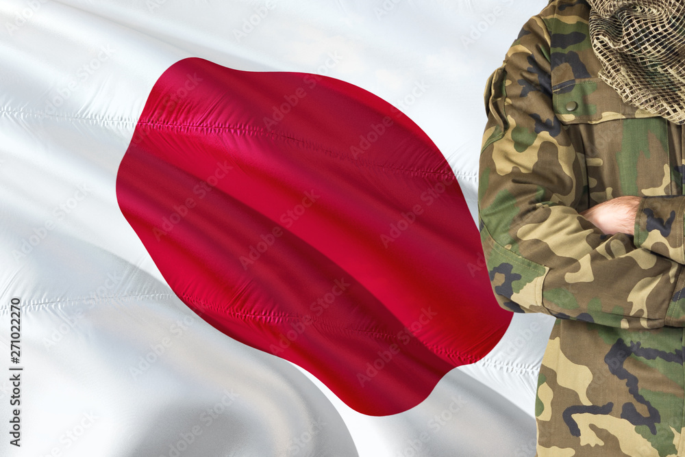 Fototapeta premium Crossed arms Japanese soldier with national waving flag on background - Japan Military theme.