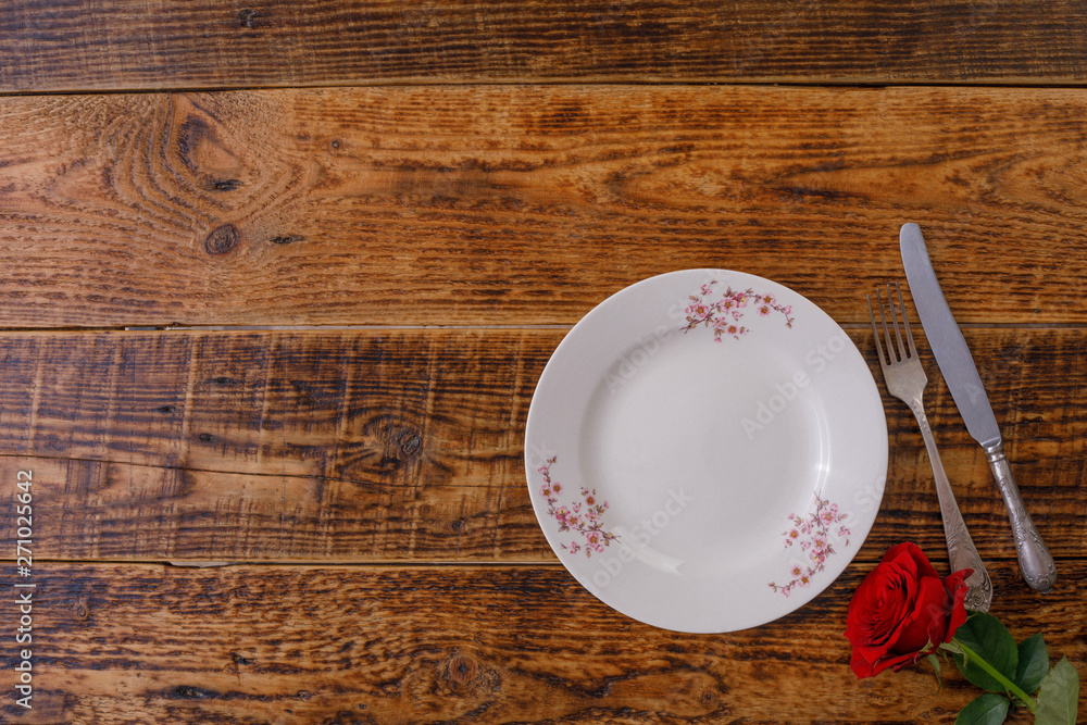 Plate and the decor of flowers on the background of vintage wooden boards. Vintage background with flower roses and place under the text. View from above. Flat lay. Cutlery. Plate and the decor of flowers on the background of vintage wooden boards. Vintage background with flower roses and place under the text. View from above. Flat lay. Cutlery.