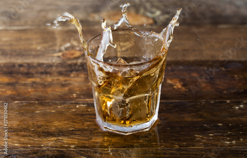 Whiskey splash. Glass of whiskey with ice cubes splashing out.
