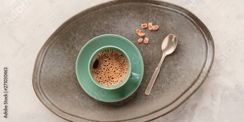 A panorama of a cup of black coffee, shot from above on a tray with caramelized sugar and a spoon, toned image
