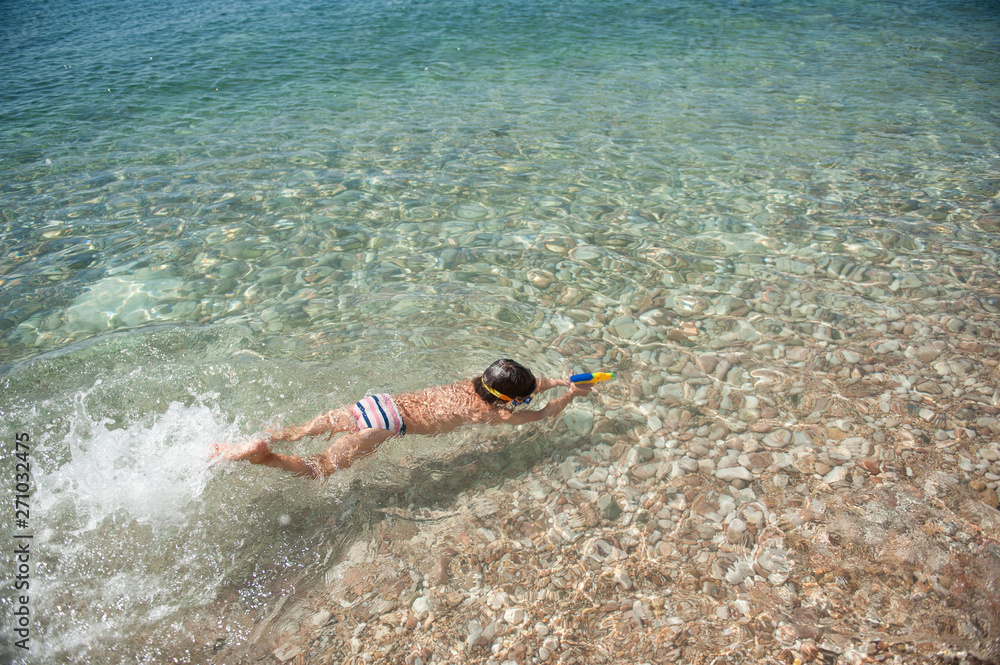 little healthy boy diving under water surface with water toy gun in summer sea