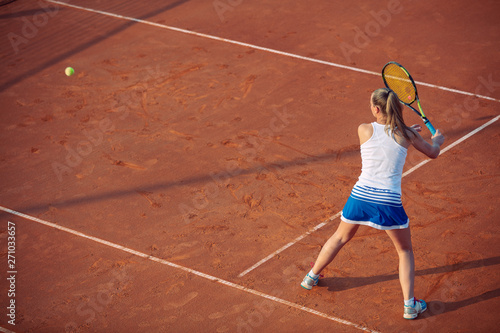 Young woman playing tennis on clay. Forehand.