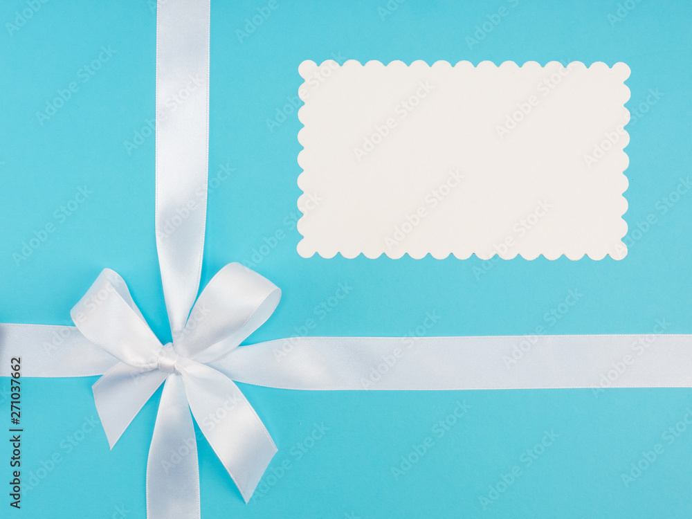 White satin ribbon with bow on blue background with white copy space. Greeting card concept