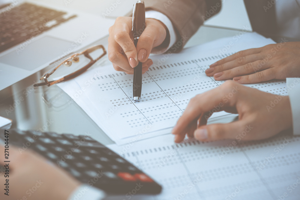 Two female accountants counting on calculator income for tax form completion hands close-up. Business and audit concept Two female accountants counting on calculator income for tax form completion hands close-up. Business and audit concept
