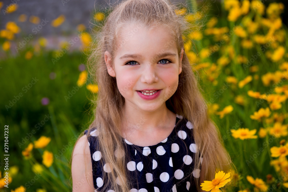 Portrait of a beautiful smiling girl outdoor. Summer portrait of a smiling girl. Little beautiful girl blonde in colors. Garden with yellow flowers, summer girl Portrait of a beautiful smiling girl outdoor. Summer portrait of a smiling girl. Little beautiful girl blonde in colors. Garden with yellow flowers, summer girl