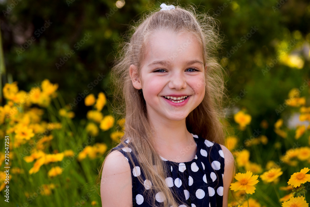 Portrait of a beautiful smiling girl outdoor. Summer portrait of a smiling girl. Little beautiful girl blonde in colors. Garden with yellow flowers, summer girl Portrait of a beautiful smiling girl outdoor. Summer portrait of a smiling girl. Little beautiful girl blonde in colors. Garden with yellow flowers, summer girl