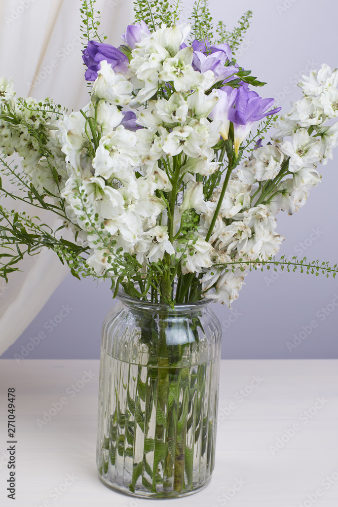 Naklejka A bouquet of white and lilac flowers in a vase on a wooden table