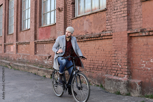 Handsome young man in grey coat and hat riding a bicycle street in the city.