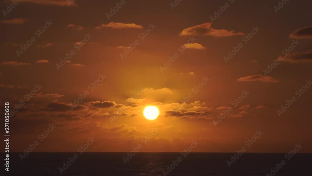 Aerial view of a sunset skies in the sea with the sun going down the horizon line with dramatic clouds in 4k