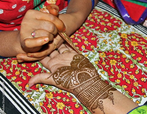 Beautiful henna or mehendi decoration on a hindu bride's hand by a henna artist, against pillow background