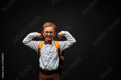 Cheerful smiling kid boy with glasses on a dark background raised his hands up demonstrating the strength and desire to win. Leadership concept of the school and supercinema.
