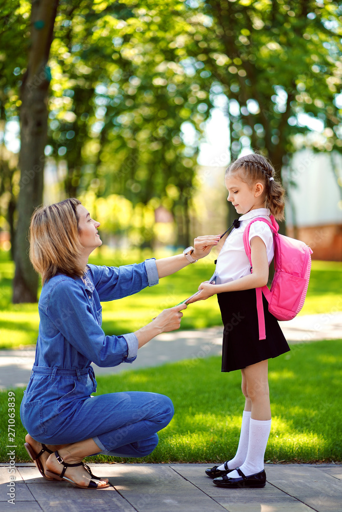 First day at school. mother leads a little child school girl in first grade. Woman and girl with backpack behind the back. Beginning of lessons. First day of fall