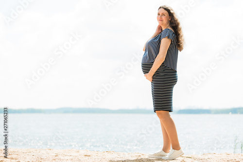 Cheerful pregnant woman with long hair standing on the beach. Happy pregnancy concept.