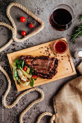 Fototapeta Naklejka Na Ścianę i Meble -  Grilled ribeye beef steak with red wine, herbs and spices on a dark stone background. Top view with copy space for your text