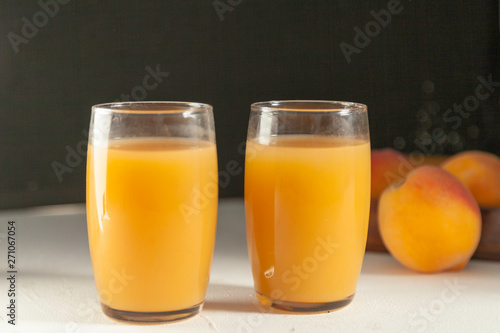 two peach juice glasses and  peaches  on white table and black backdrop