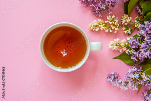 Cup of tea with lilac flower on a pink background