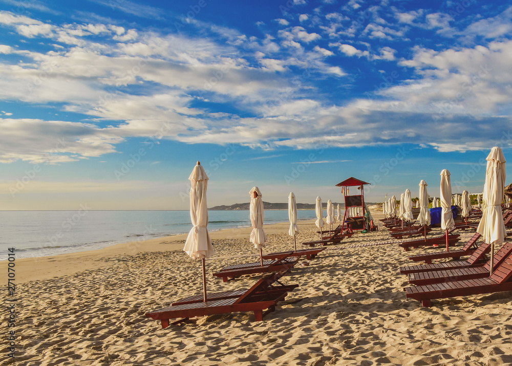Sun loungers and umbrellas on an empty sandy beach. Summer sunny cloudy blue sky. Cam Ranh. Vietnam.