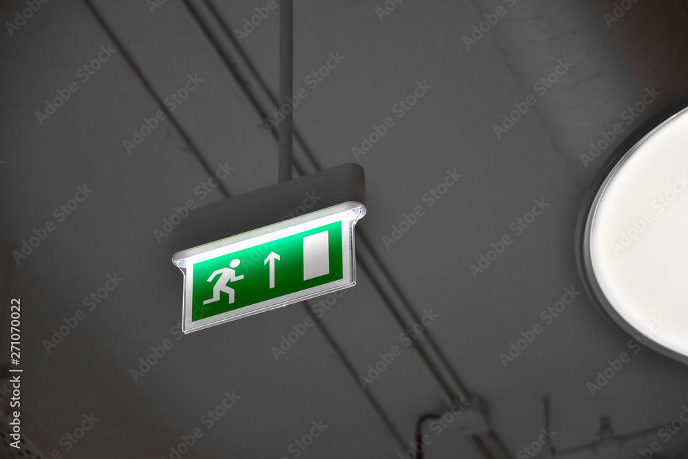 illuminated green exit sign suspended from the ceiling in a public facility