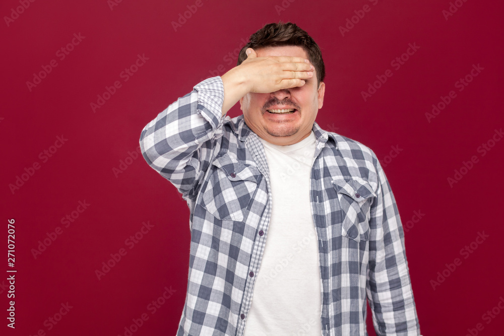 Portrait of shocked handsome middle aged business man in casual checkered shirt standing, closed his eyes with hand and do not want to see something. studio shot, isolated on dark red background. Portrait of shocked handsome middle aged business man in casual checkered shirt standing, closed his eyes with hand and do not want to see something. studio shot, isolated on dark red background.