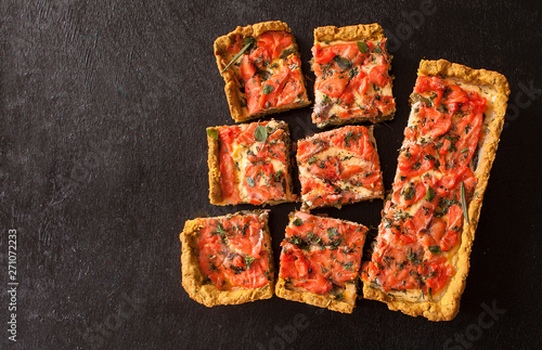 Rectangular quiche with salmon, spinach and cream on a black wooden table. French cuisine. The view from the top. Copy space.