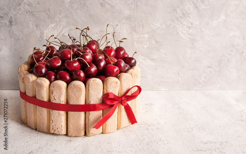 Summer cake of French savoyardi cookies with whipped cream, decorated with fresh cherry berries. Free space for text photo