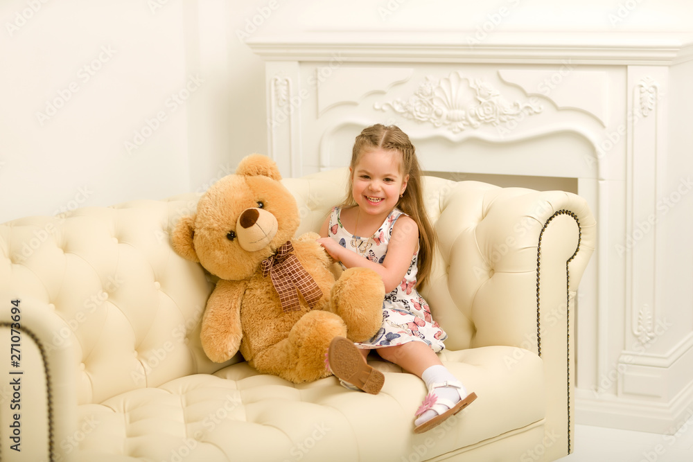 Little girl on sofa hugging teddy bear. Stock Photo | Adobe Stock