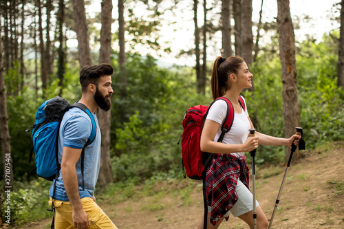 Couple of young happy travelers hiking with backpacks on the beautiful forest trail