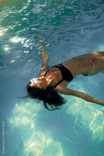 Brunette caucasian model in bikini floating in the pool water