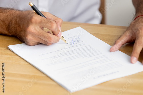 Close up caucasian male hands holding pen singing business paper