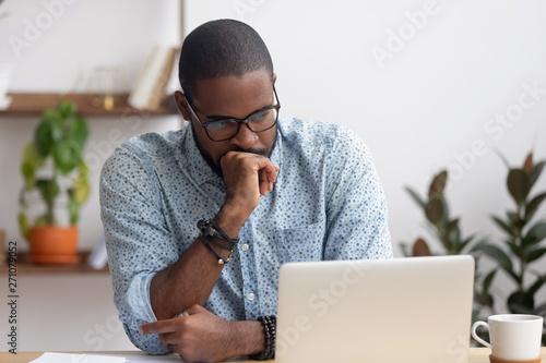Foto Head shot serious puzzled African American businessman looking at laptop