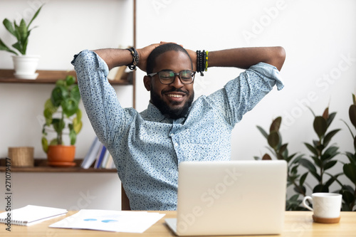 Fotografie Smiling Afro-American businessman holding hands behind head sitting at office