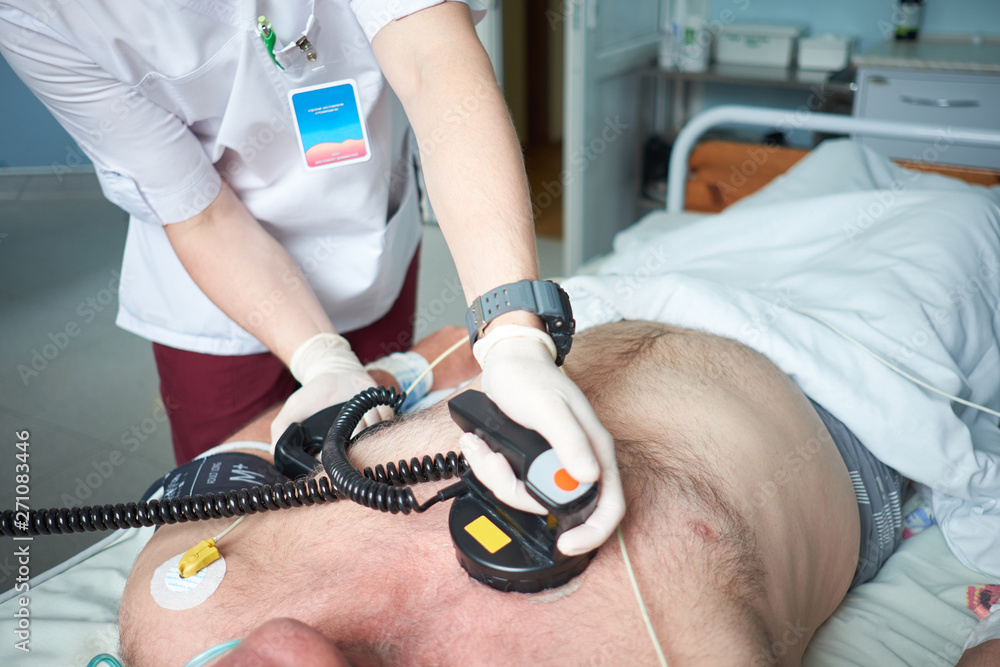 Doctor intensivist performs defibrillation to critical patient - obrazy, fototapety, plakaty 