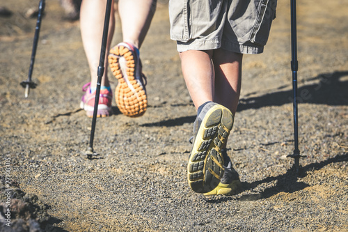 Close up back view of mother and son feet walk on a mountain path with trekking shoes and hiking poles Frog perspective of a couple with walking sticks Travel adventure, nomad and health concept