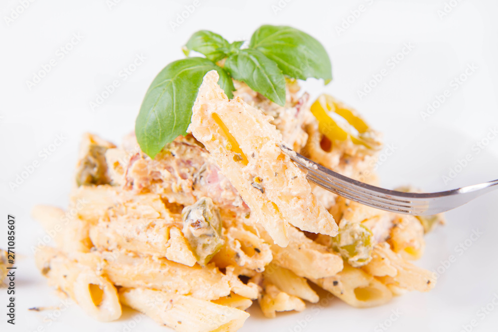 Pasta eaten with a fork - penne with white cream sauce with bacon and jalapeño peppers on a plate, decorated with fresh basil Pasta eaten with a fork - penne with white cream sauce with bacon and jalapeño peppers on a plate, decorated with fresh basil