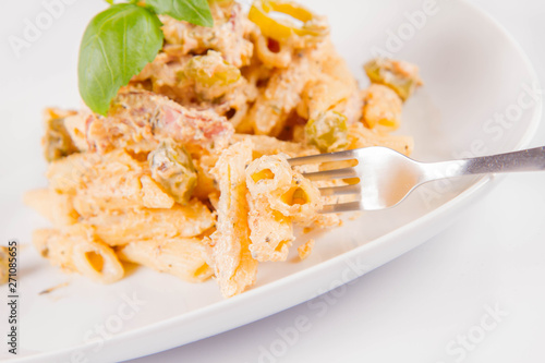 Pasta eaten with a fork - penne with white cream sauce with bacon and jalapeño peppers on a plate, decorated with fresh basil 