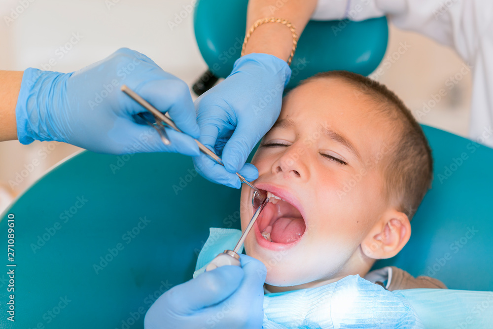 Dentist is treating a boy's teeth. Dentist examining boy's teeth in clinic. A small patient in the dental chair smiles. Dantist treats teeth Dentist is treating a boy's teeth. Dentist examining boy's teeth in clinic. A small patient in the dental chair smiles. Dantist treats teeth