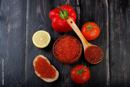 red caviar on wooden cup, wooden spoon and vegetables on wooden background. top view