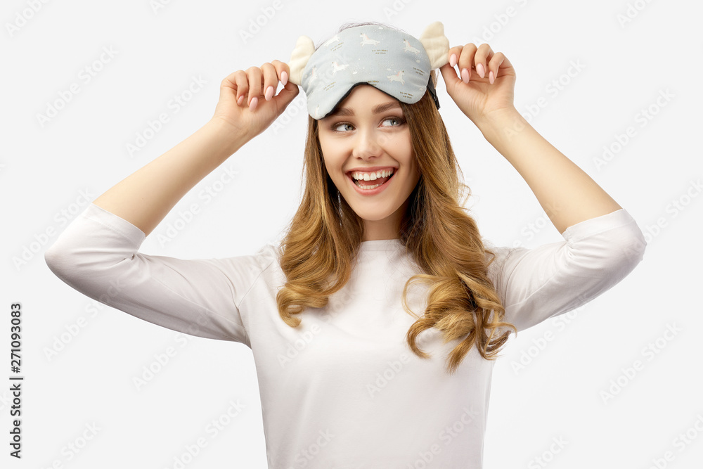 pretty young brunette woman smiles cheerfully and holds both hands on a sleep mask. Concept of rest and healthy sleep. Studio portrait on isolated background pretty young brunette woman smiles cheerfully and holds both hands on a sleep mask. Concept of rest and healthy sleep. Studio portrait on isolated background